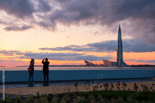 Tourists on the promenade photograph a beautiful sunset over the Baltic sea. View of the tallest building in Europe. St. Petersburg, Russia. © Andrei Stepanov