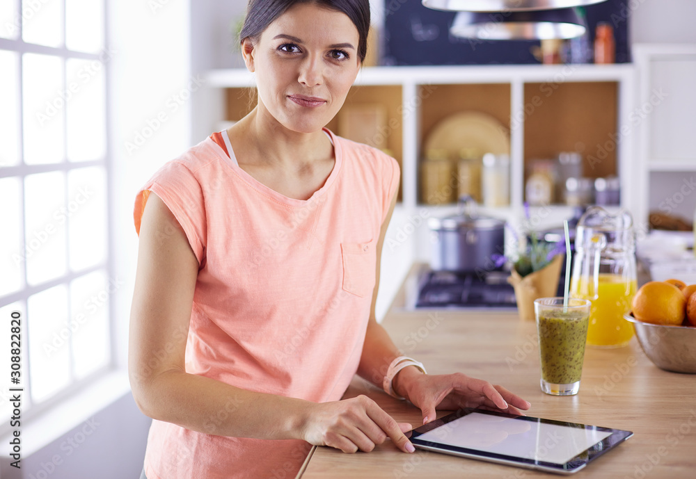 Beautiful young woman using a digital tablet in the kitchen