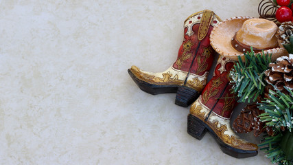 brown and tan rustic cowboy boots and hat with christmas decorations laying  on a tan background with copy space