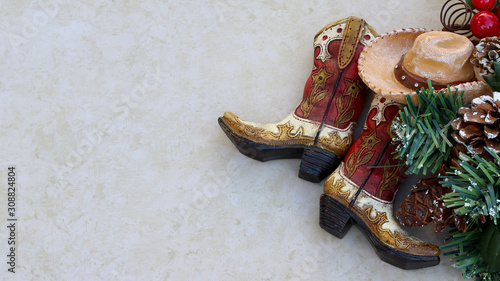 brown and tan rustic cowboy boots and hat with christmas decorations laying  on a tan background with copy space