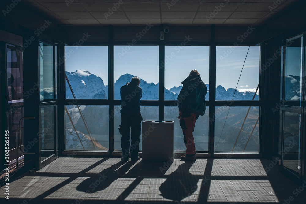 People Silhouettes Stand near Glass Wall on Background of Alpine Mountains People Silhouettes Stand near Glass Wall on Background of Alpine Mountains