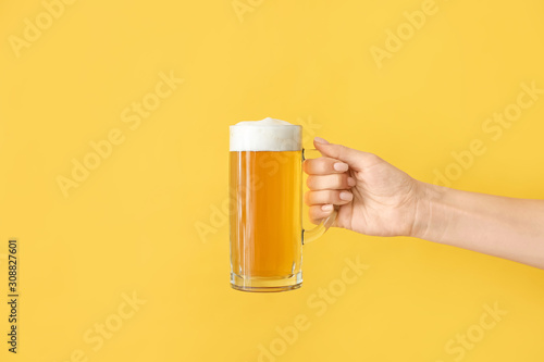 Hand with mug of beer on color background