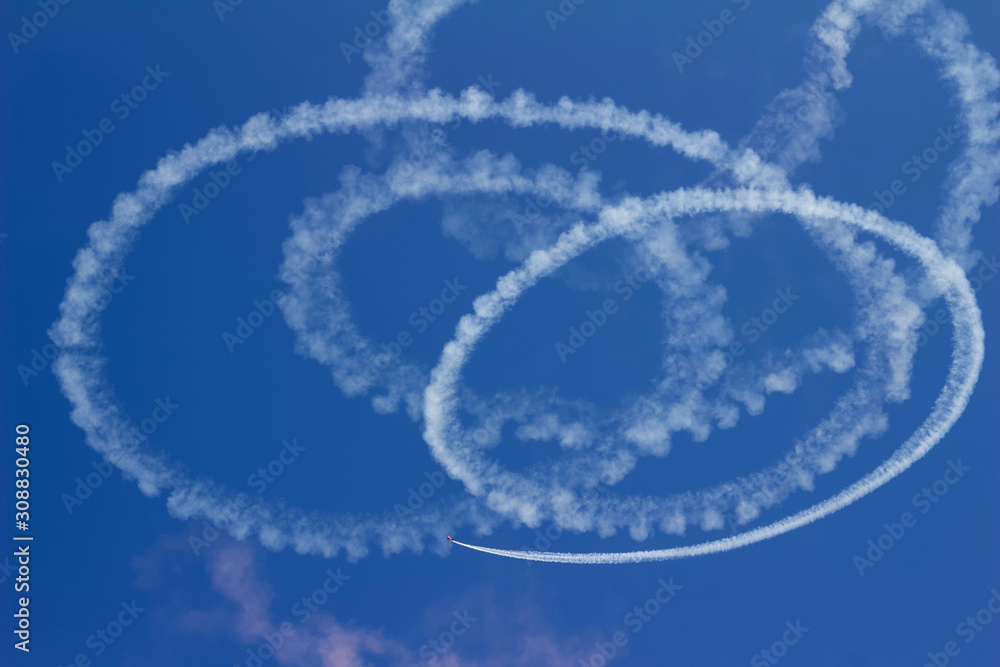 Abstract view of the vapor trail of an airplane skywriting in spiraling circles against a deep blue sky