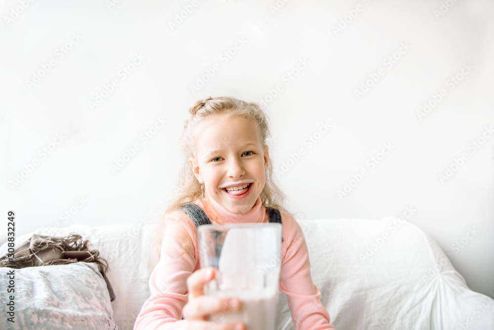 Girl drinks kefir or milk for breakfast. funny mustache. laughing on the couch at home. healthy eating children Girl drinks kefir or milk for breakfast. funny mustache. laughing on the couch at home. healthy eating children