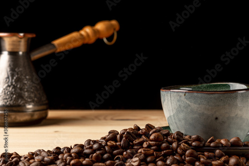 Handmade cup with coffee on the table. Countertop made of wood. Coffee beans. Black background.
