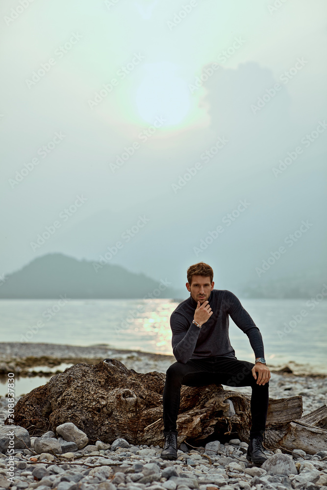 Autumn photo of young fashionable male model wear turtleneck and posing outdoor near the mountains and lake