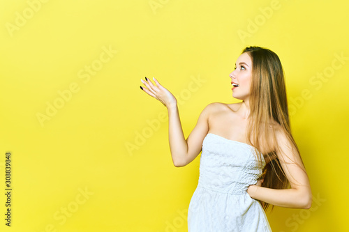 Portrait of a cheerful young lady smiling presenting your product. Woman points to copyspace. Isolated on a yellow background.