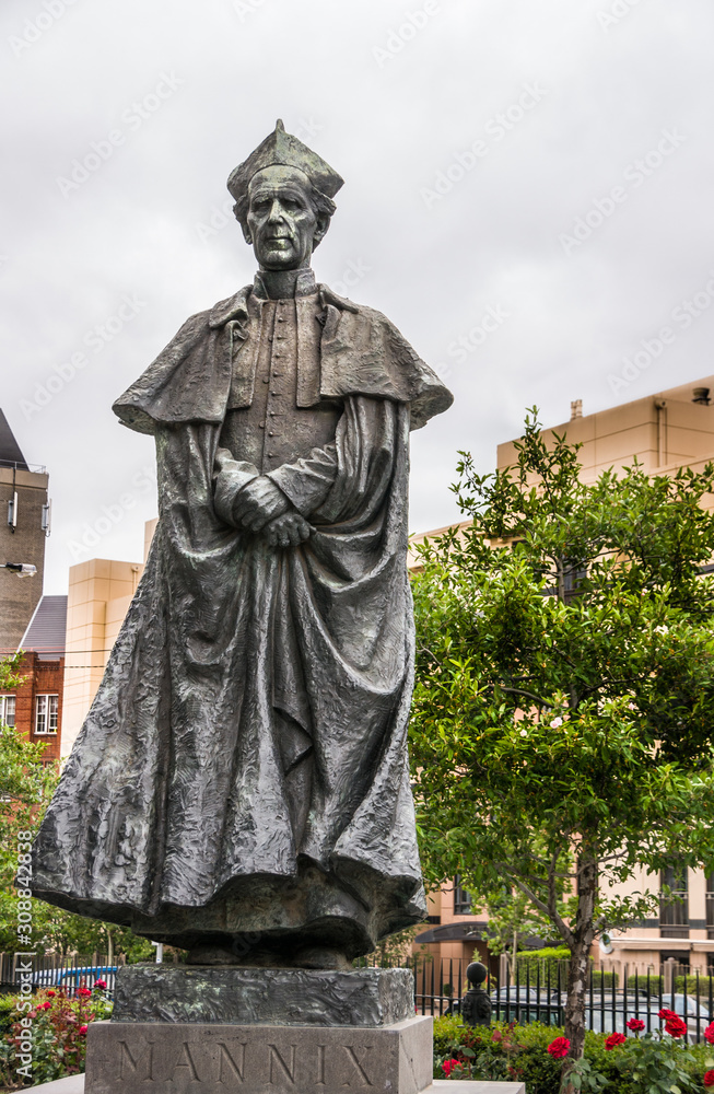 Melbourne, Australia - November 16, 2009: Closeup of Gray bronze statue of Archbishop Daniel Mannix on side of Saint Patricks Cathedral. Green foliage and red roses.