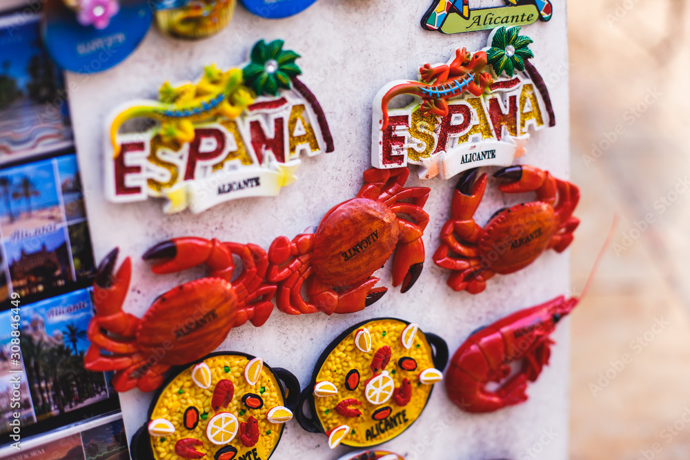Obraz premium View of traditional tourist souvenirs and gifts from Spain, Alicante, Valencia with toys, bull figures, flamenco dancer dolls, fridge magnets with and key ring keychain, in local vendor souvenir shop
