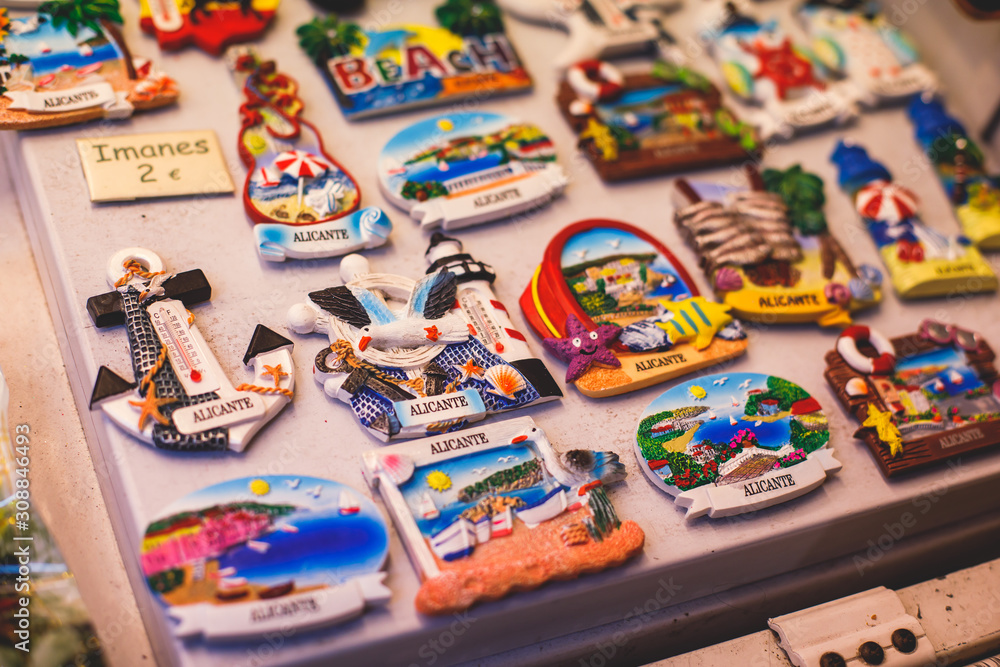 Fototapeta premium View of traditional tourist souvenirs and gifts from Spain, Alicante, Valencia with toys, bull figures, flamenco dancer dolls, fridge magnets with and key ring keychain, in local vendor souvenir shop