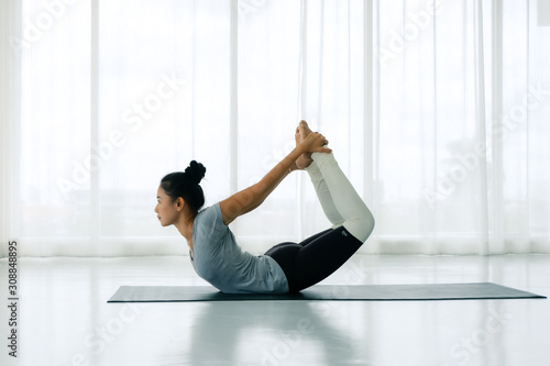Side view portrait of Beautiful Asian woman working out in fitness club or at home, doing yoga or pilates exercise. Dhanurasana, Bow pose,Full length, Concept of healing body and spirit © Nipapun