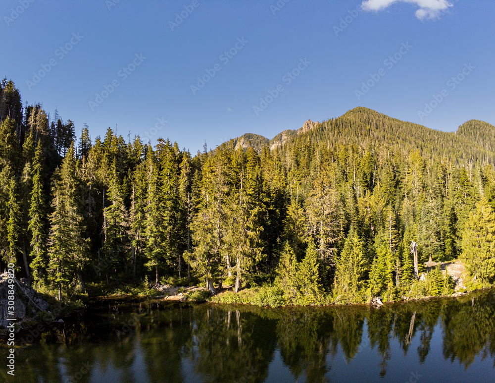 Secluded Kelcema Lake and the surrounding mountain and trees reflecting in the shaded water on a clear summer afternoon in the Mount Baker-Snoqualmie National Forest in Silverton Washington State