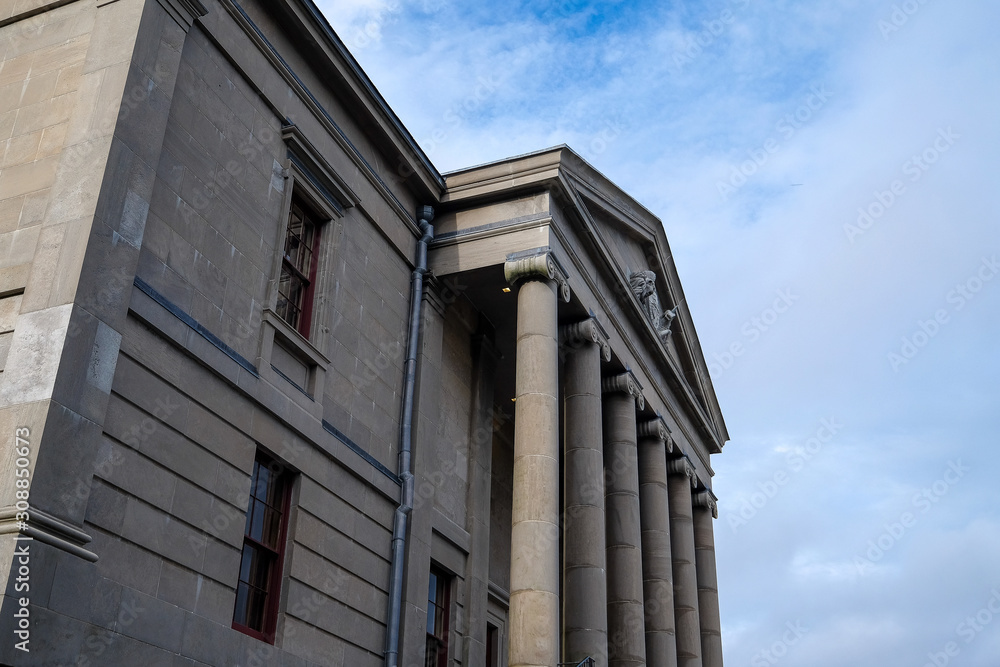 Side view of a court house building with tall pillars and windows. The sky is blue in the background with some clouds. Side view of a court house building with tall pillars and windows. The sky is blue in the background with some clouds.