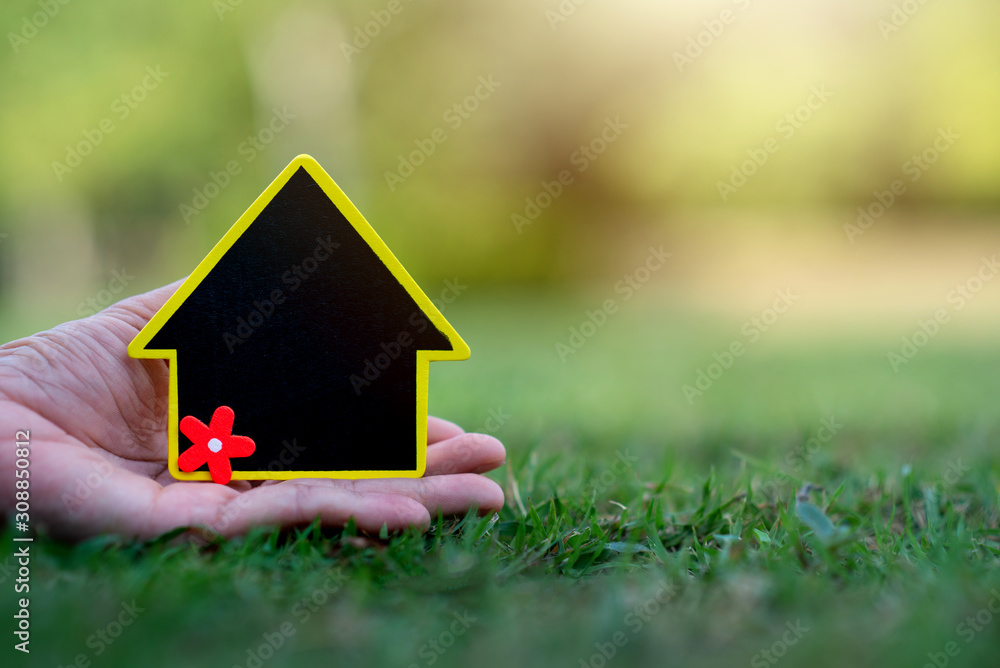 Hand holding mini house on the grass Hand holding mini house on the grass