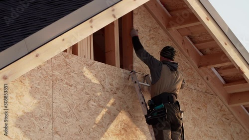 Builder is adjusting triangle plywood on its place. Frame house under construction