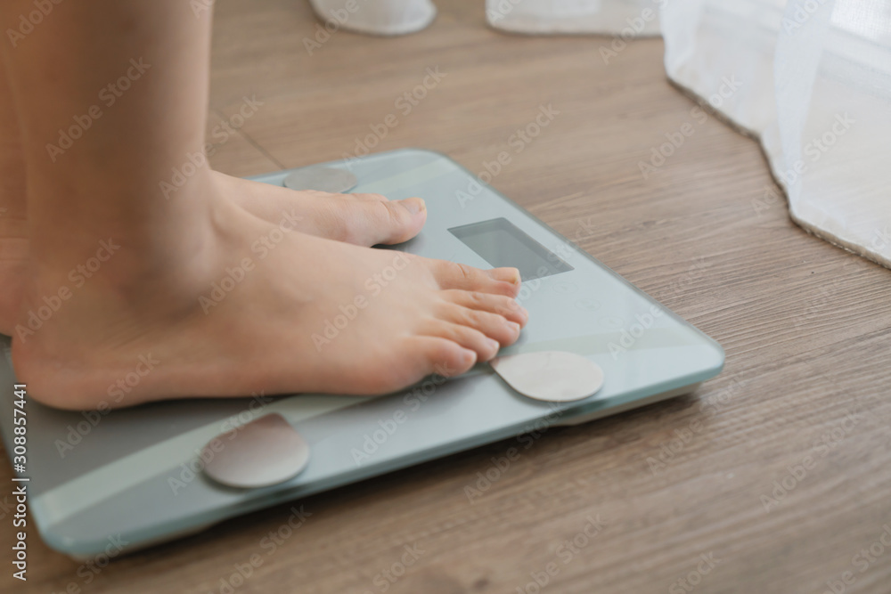 Fototapeta premium feet on digital weighing scale on wooden floor
