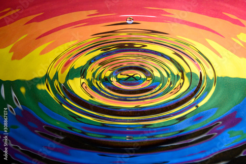 A single water droplet falling towards the centre of a water splash reflecting the Rainbow Pride Extinction Rebellion flag and logo