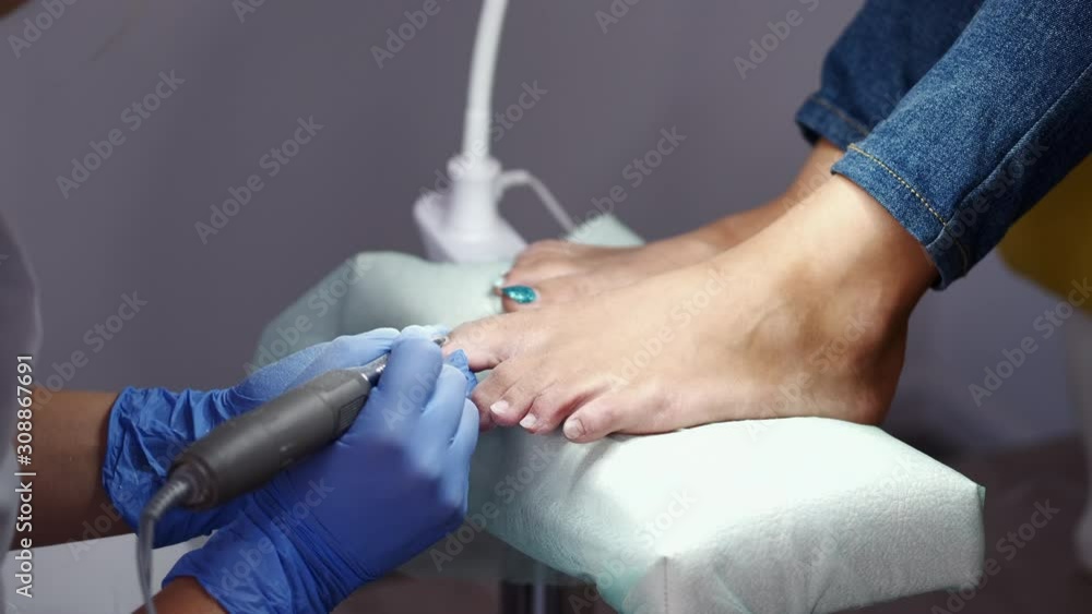 The pedicure master is polishing nails by the cutter. The girl who is a customer is sitting in a pedicure stoel while the procedure. The pedicure master is polishing nails by the cutter. The girl who is a customer is sitting in a pedicure stoel while the procedure.
