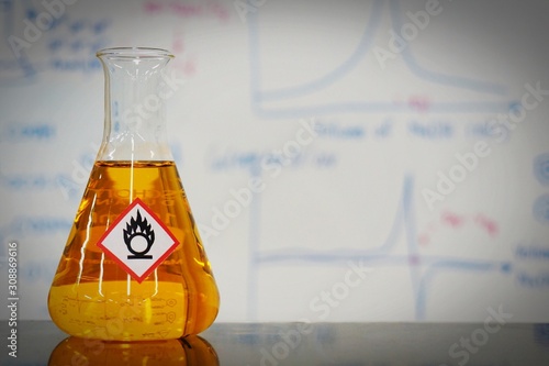 Erlenmeyer flask with Orange liquid and chemical hazard warning symbols labels (oxidizing agent sign) on whiteboard with chemical learning background.
