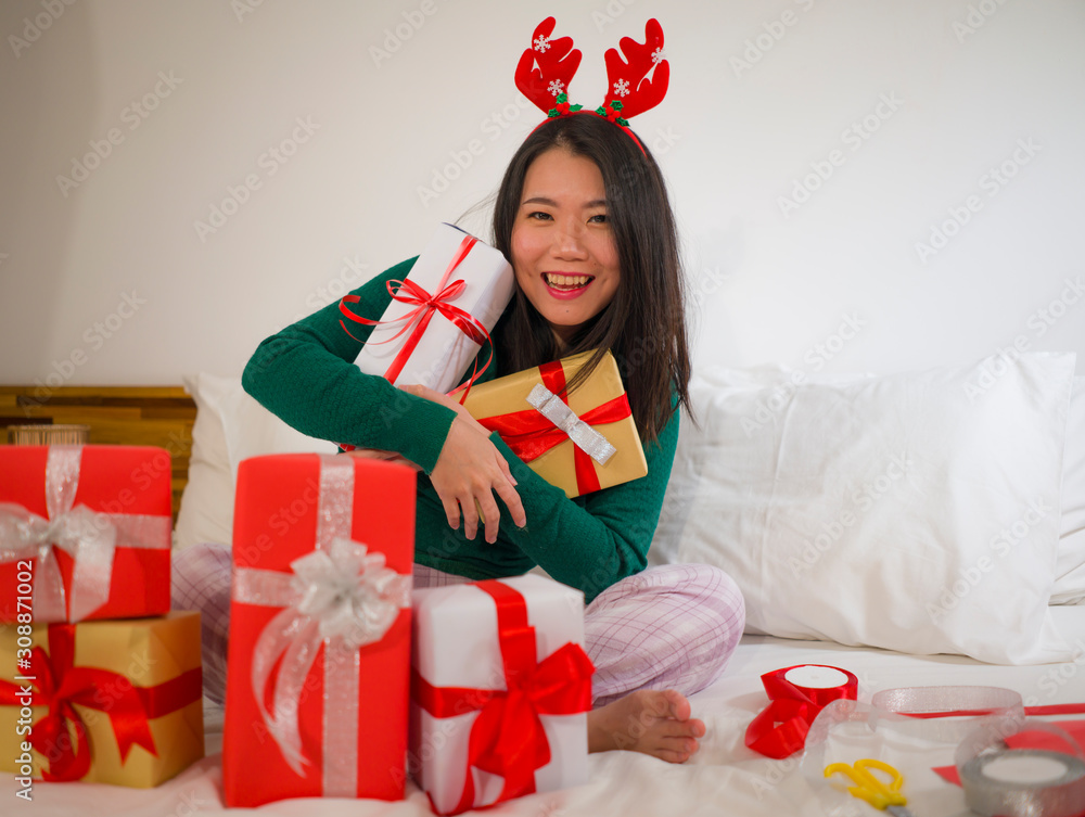 Christmas holiday lifestyle portrait of young happy and beautiful Asian Korean woman on bed in sweet reindeer horns preparing xmas presents wrapping gift boxes enjoying Christmas holiday lifestyle portrait of young happy and beautiful Asian Korean woman on bed in sweet reindeer horns preparing xmas presents wrapping gift boxes enjoying