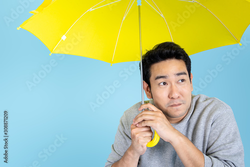 Happy Asian man holding yellow umbrella on blue background. photo