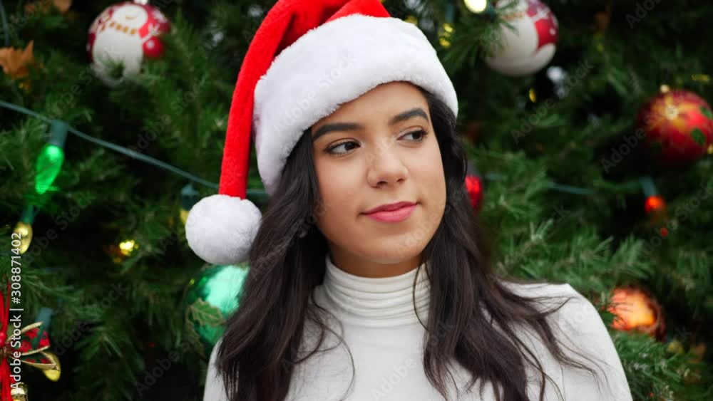 A beautiful woman in a Santa Claus hat dancing and celebrating the holiday season with a decorated Christmas tree and ornaments. A beautiful woman in a Santa Claus hat dancing and celebrating the holiday season with a decorated Christmas tree and ornaments.