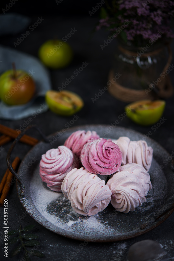 Delicious homemade berry marshmallows with powdered sugar lies in a tin plate on a gray table. Vertical photo.