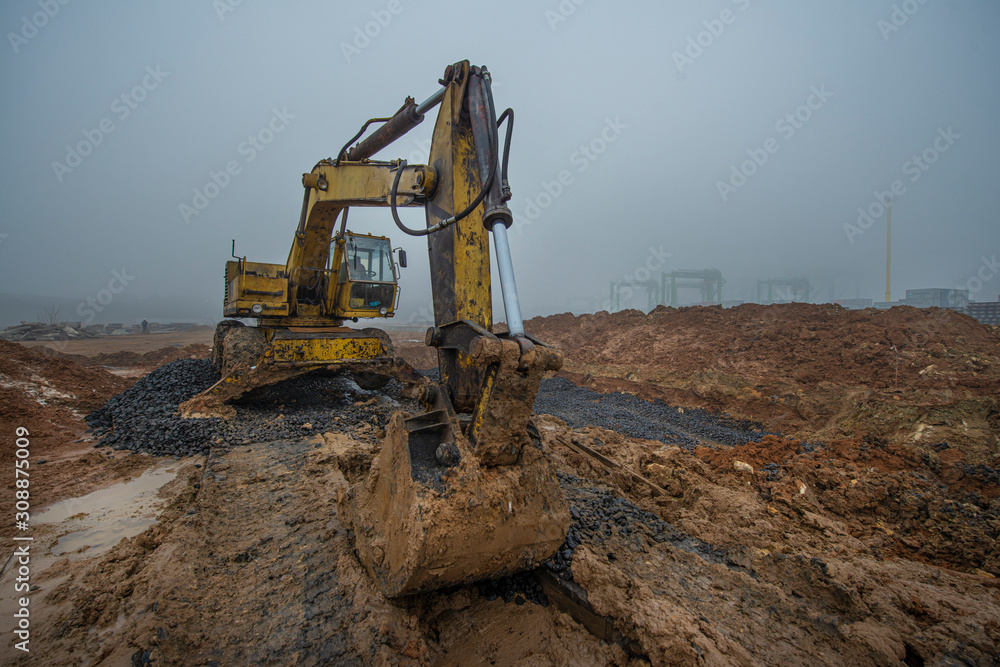 Obraz premium This is an excavator at a construction site on the background of clay soil