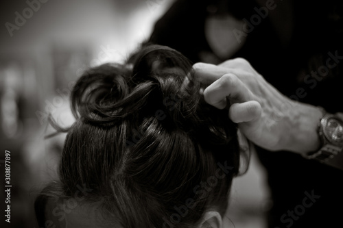 Black and white photo of a Hairdresser doing a woman's hair in professional hairdressing salon or barbershop , seen from behind the customer, unrecognizable.