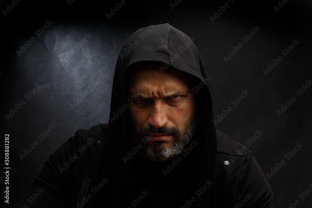 Portrait of a bald man with a beard in a black hood on a dirty gray background. Portrait of a bald man with a beard in a black hood on a dirty gray background.