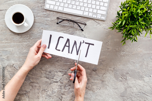 Motivation to be confident. Hands cut text I can't with scissors on grey office desk photo