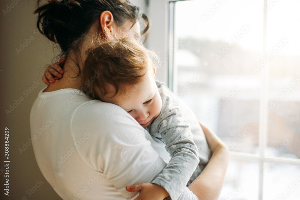 © Galina Zhigalova - Young woman mom with baby girl on hands near window at home
