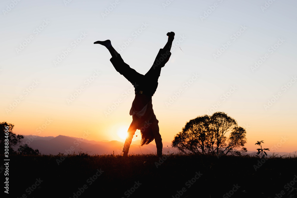 Silhouette happy child playing upside down outdoors in summer park walking on hands at sunset