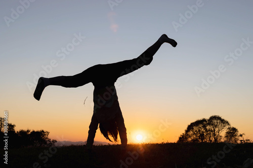 Fototapeta Naklejka Na Ścianę i Meble -  Silhouette happy child playing upside down outdoors in summer park walking on hands at sunset