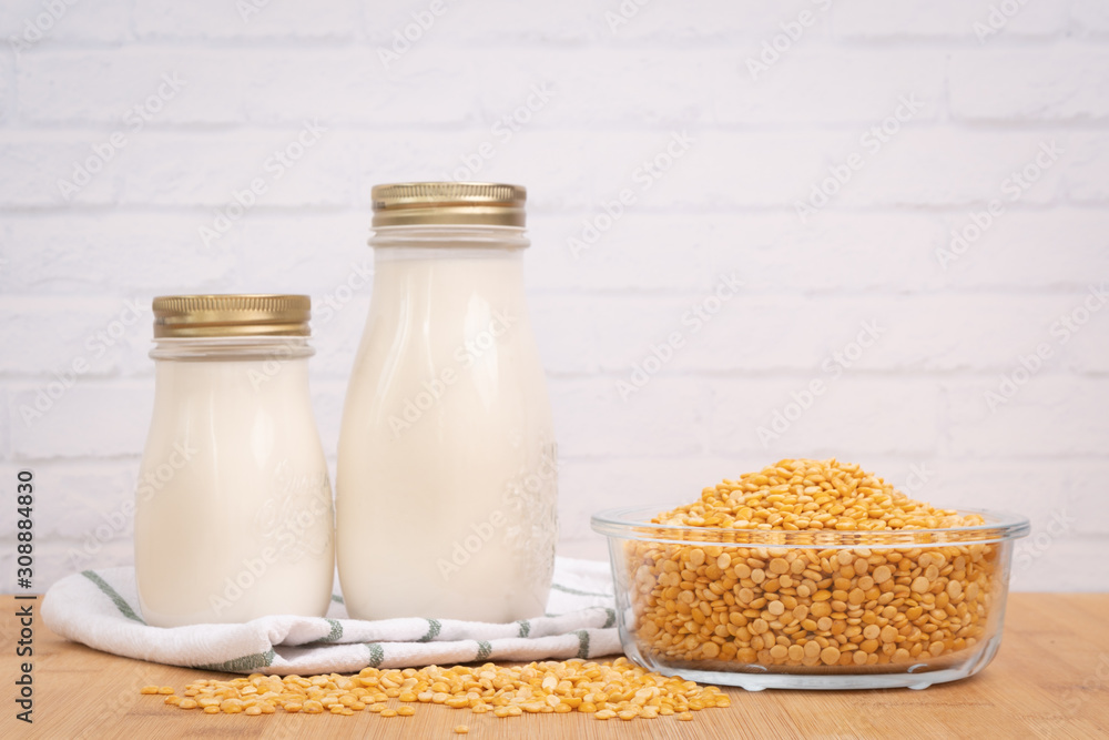 Fresh homemade oat milk in glass bottles set beside a pile of rolled oats in a bowl on the wooden kitchen table. Oat milk or plant milk are high protein and dairy-free, rich in vitamins and nutrition Fresh homemade oat milk in glass bottles set beside a pile of rolled oats in a bowl on the wooden kitchen table. Oat milk or plant milk are high protein and dairy-free, rich in vitamins and nutrition