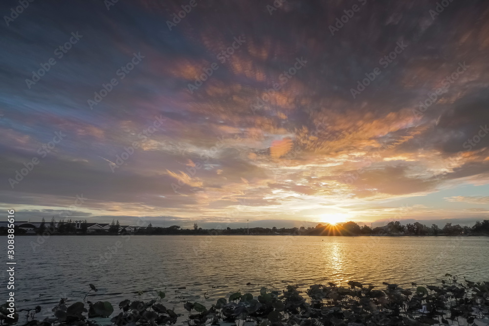 Lake view evening of dark clouds moving above lotus lake with yellow sun light in rainy sky background, sunset at Krajub reservoir, Ban Pong District, Ratchaburi, Thailand. (Clouds Stack Technic) Lake view evening of dark clouds moving above lotus lake with yellow sun light in rainy sky background, sunset at Krajub reservoir, Ban Pong District, Ratchaburi, Thailand. (Clouds Stack Technic)
