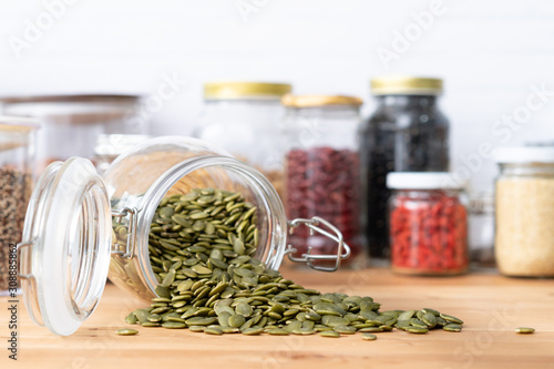 Φωτογραφία Beautiful closeup of a pile of dried pumpkin or pepita seeds pour out from a glass jar airtight container on the wooden kitchen counter