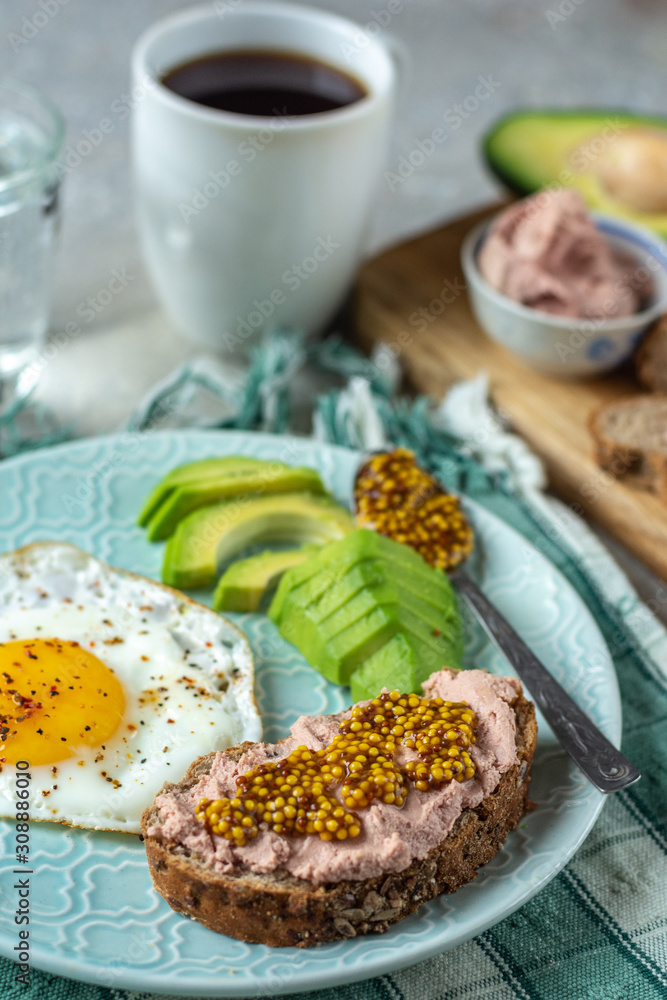 Healthy breakfast with cooked egg, chopped avocado on a plate, cereal bread with French mustard paste, a glass of water with coffee Healthy breakfast with cooked egg, chopped avocado on a plate, cereal bread with French mustard paste, a glass of water with coffee