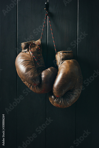 Vintage brown box gloves, hanging on black wooden wall in dramatic lighting.