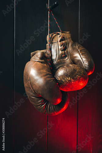 - Old brown boxing gloves, hanging on black wooden wall in dramatic red lighting. Copy space. © a_khachatryan