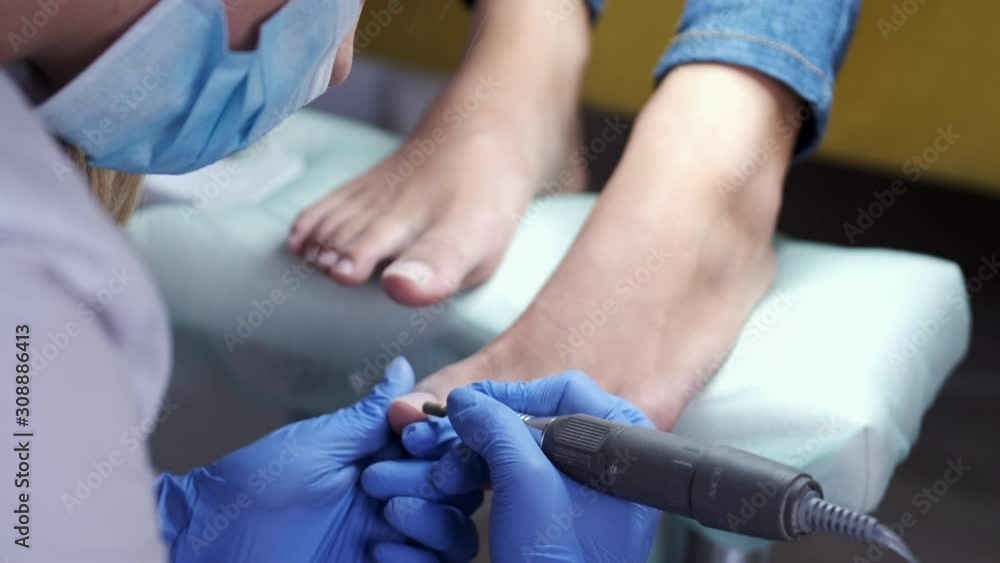 The pedicure master is polishing nails by a milling cutter. The nail technician is removing cuticle from nails. She is using a milling cutter. The customer's feet are on the special pillow. The pedicure master is polishing nails by a milling cutter. The nail technician is removing cuticle from nails. She is using a milling cutter. The customer's feet are on the special pillow.