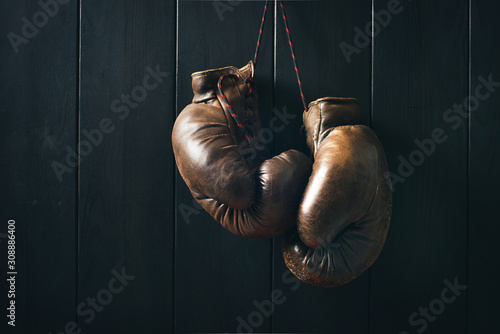 Vintage brown boxing gloves, hanging on black wooden wall in dramatic lighting. Copy space. © a_khachatryan