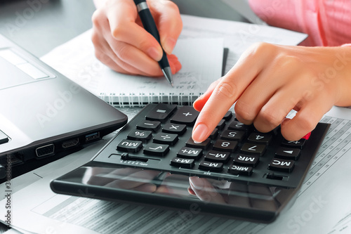 Female accountant in the office uses a calculator and writes data in a notebook. Profit analysis, taxes and payments calculations, preparation of financial statements concept photo