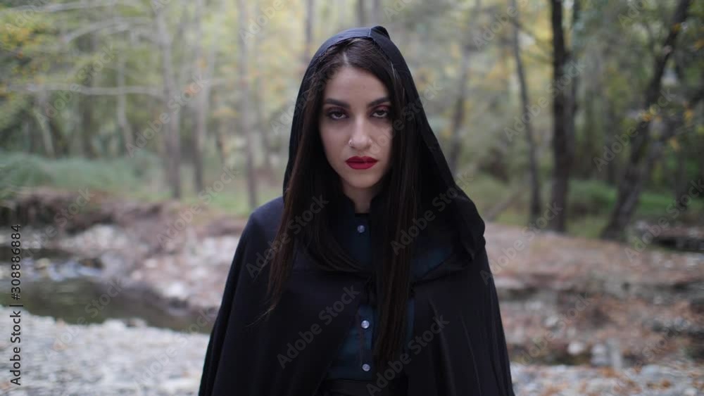Portrait of a mysterious beautiful woman in a dark cloak as she looks up and stares deeply into the camera in slow motion. Portrait of a mysterious beautiful woman in a dark cloak as she looks up and stares deeply into the camera in slow motion.