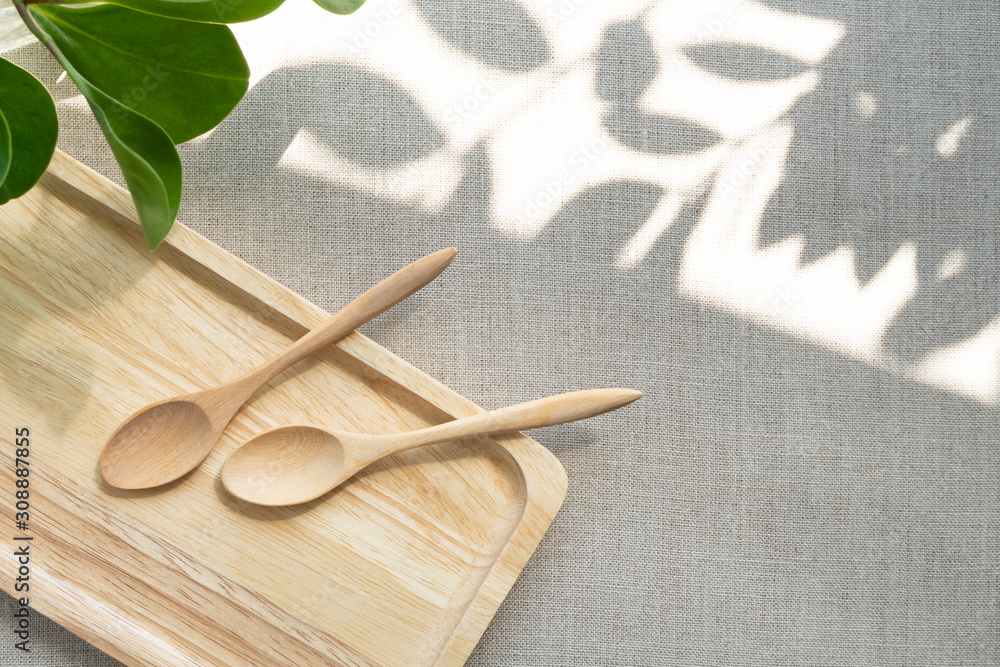 A blank wooden tray with spoons neatly arranging on linen table cloth, with the space showing sunlight and beautiful leaves shadow. Background with copy space for well being and minimal products. A blank wooden tray with spoons neatly arranging on linen table cloth, with the space showing sunlight and beautiful leaves shadow. Background with copy space for well being and minimal products.