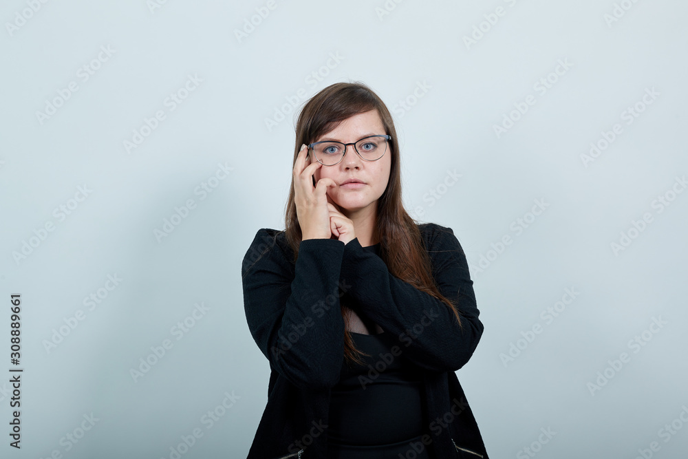 Young pretty attractive woman looking directly, opened eyes with the hand on the cheek on isolated gray background wearing fashion clothes Young pretty attractive woman looking directly, opened eyes with the hand on the cheek on isolated gray background wearing fashion clothes