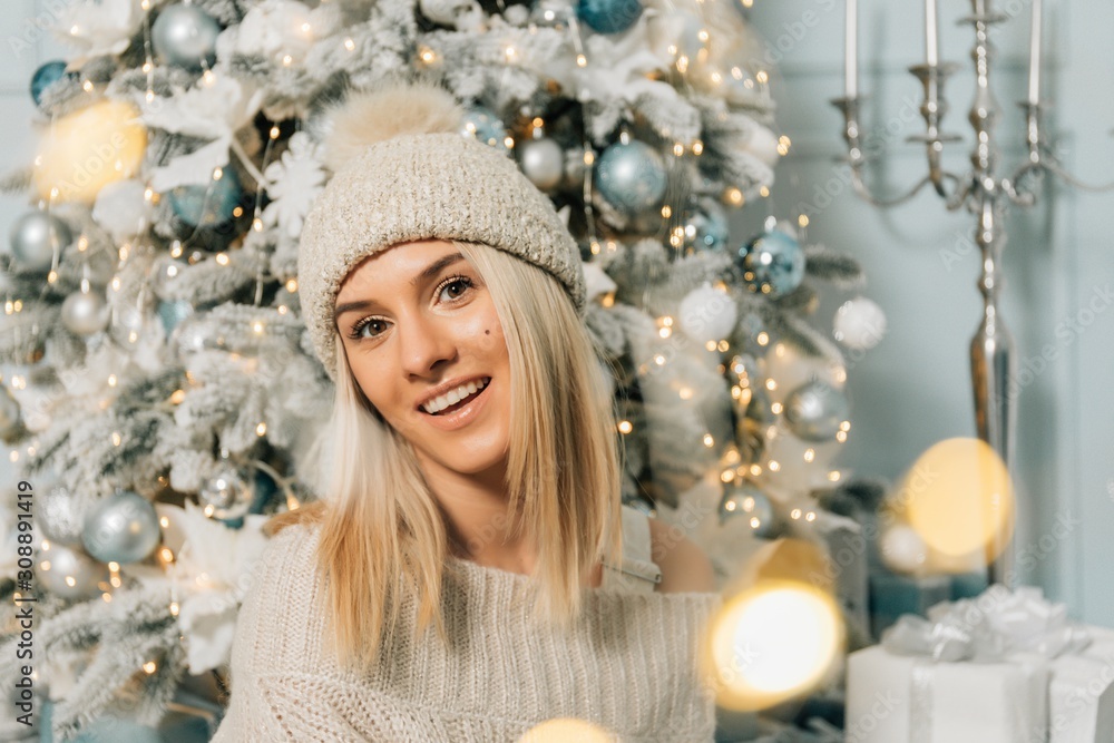 Christmas fashion photo of beautiful girl with blond hair in cozy clothes posing near New Year tree with presents Christmas fashion photo of beautiful girl with blond hair in cozy clothes posing near New Year tree with presents