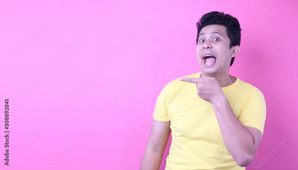 Obraz premium A young Asian man pointed an astounding and astounding hand and face on the pink background in the studio with copy space.
