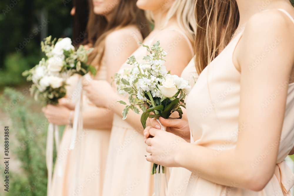 Glorious bridesmaids in light dresses  holding beautiful flowers