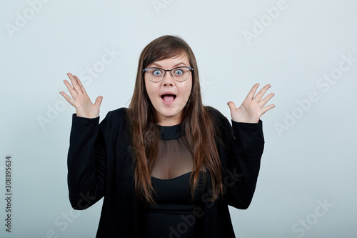 Surprised cheerful young woman in casual black dress, opened mouth, spreading hands isolated on gray background in studio. People sincere emotions, lifestyle concept. photo